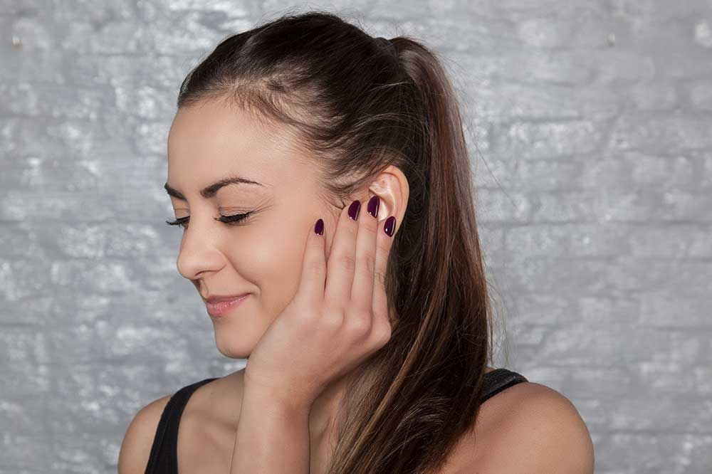 Young woman gently touching her ear over a full, clogged feeling, a concern Island Better Hearing evaluates in Melville, N